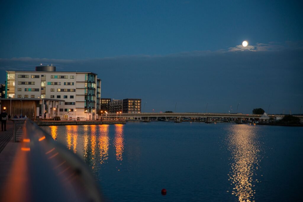 Scenic night view of a waterfront cityscape with moonlit reflections on the river.
