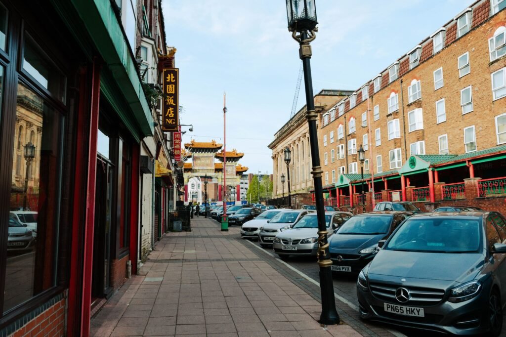 Vibrant street in Liverpool's Chinatown featuring cars, storefronts, and traditional architecture.