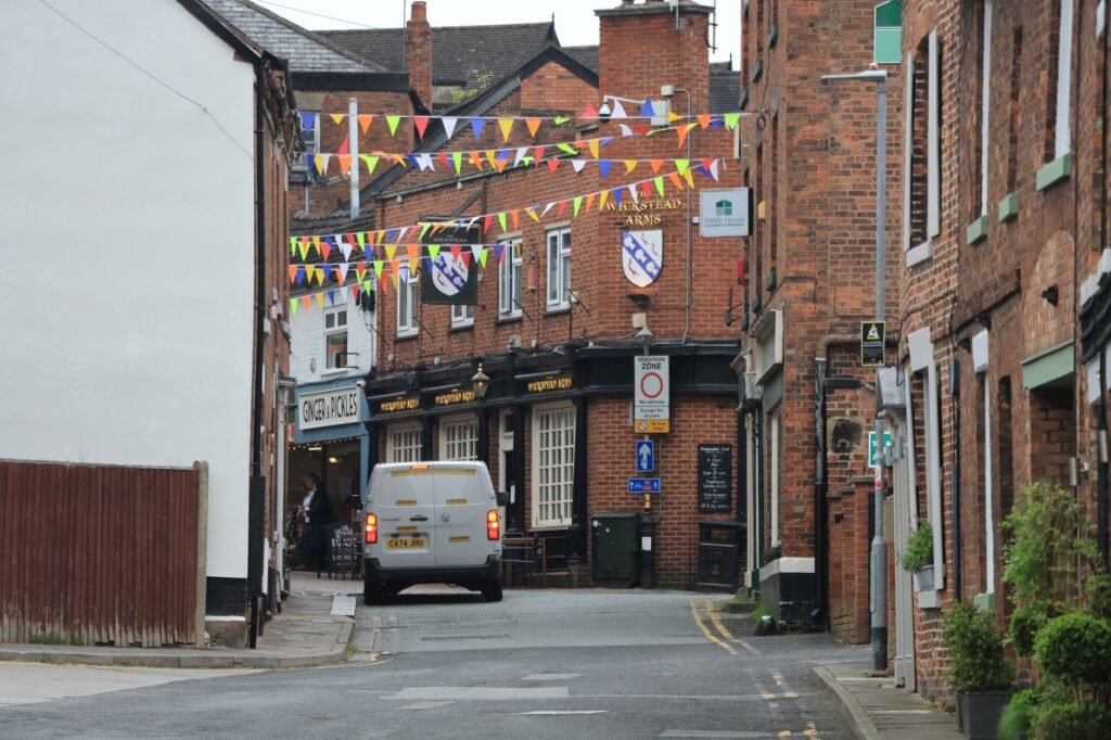 A quaint street in Nantwich, England, adorned with vibrant bunting above brick buildings and a classic pub.
