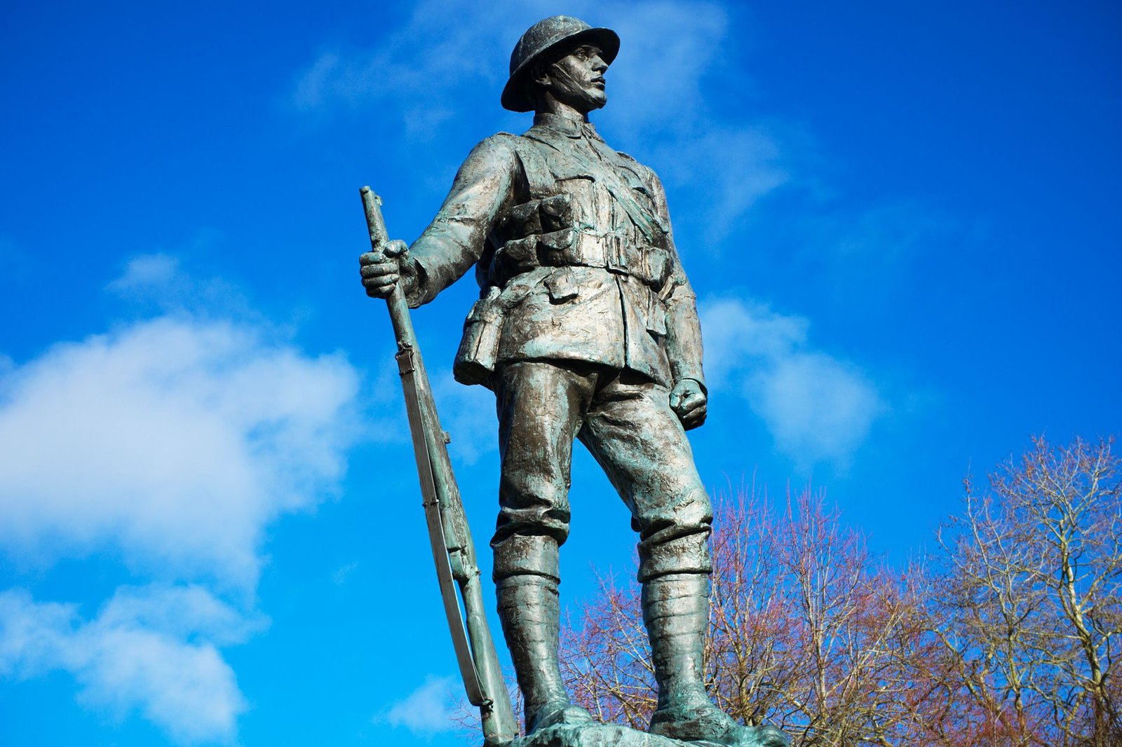 A striking bronze statue of a World War I soldier in Winchester against a bright blue sky.