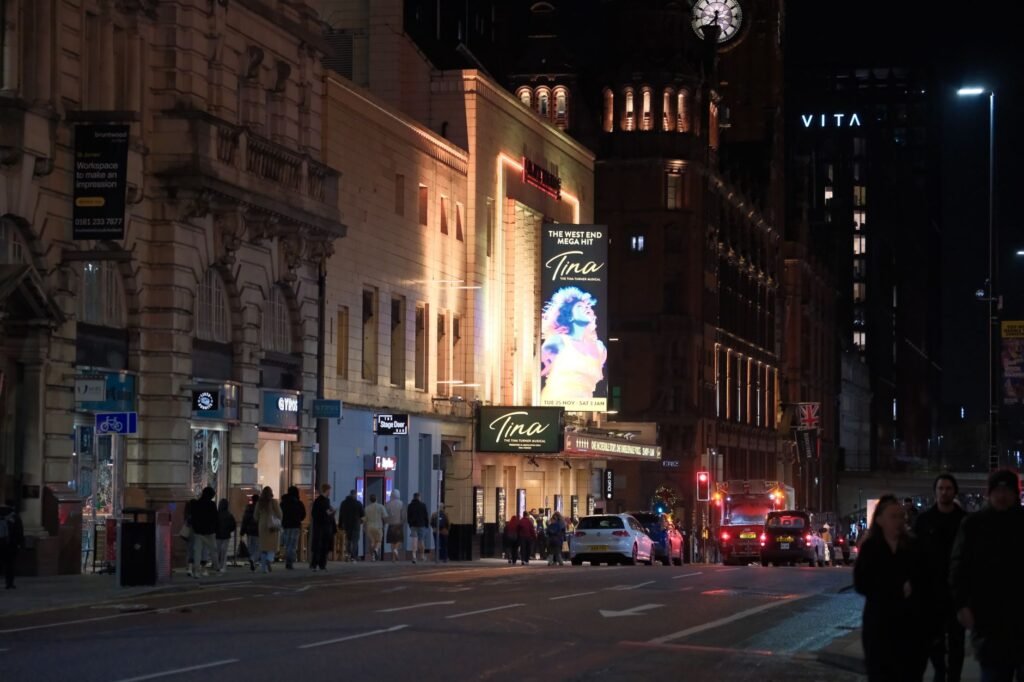 A bustling city street at night featuring a theater with bright lights and busy pedestrian activity.