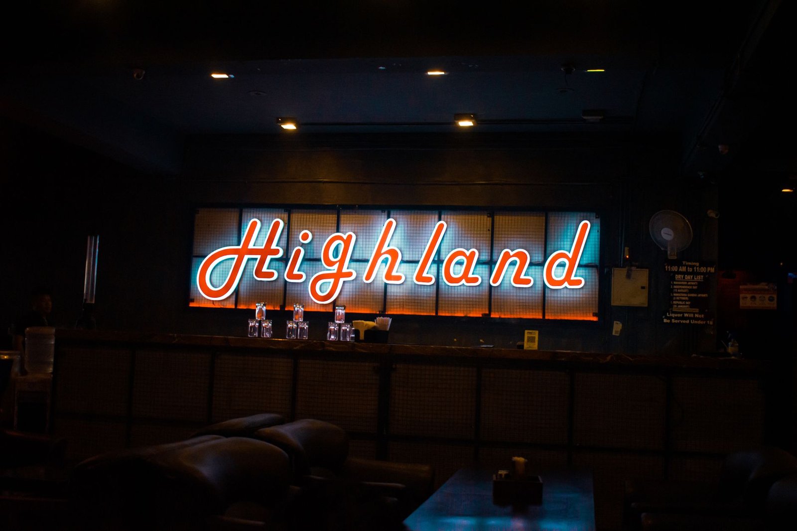 A neon sign reading 'Highland' illuminates a cozy, dark bar interior, creating a vibrant nightlife atmosphere.