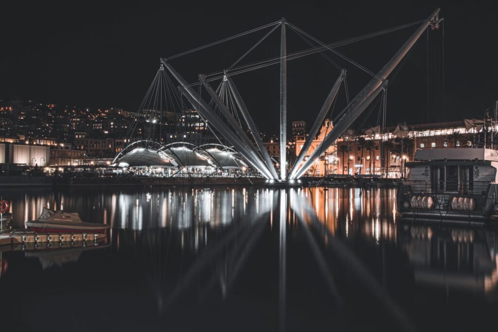 Night scene of Genoa harbor featuring the iconic Bigo structure reflected in the water.