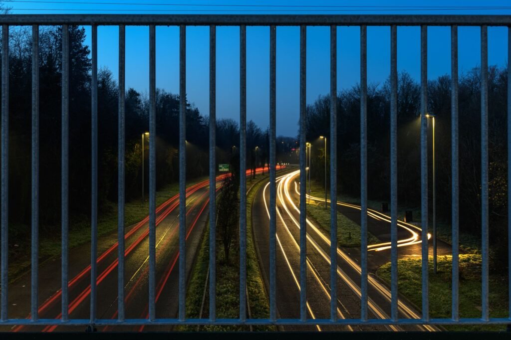 Long exposure of a highway's light trails through a guardrail at dusk in Craigavon, Northern Ireland.