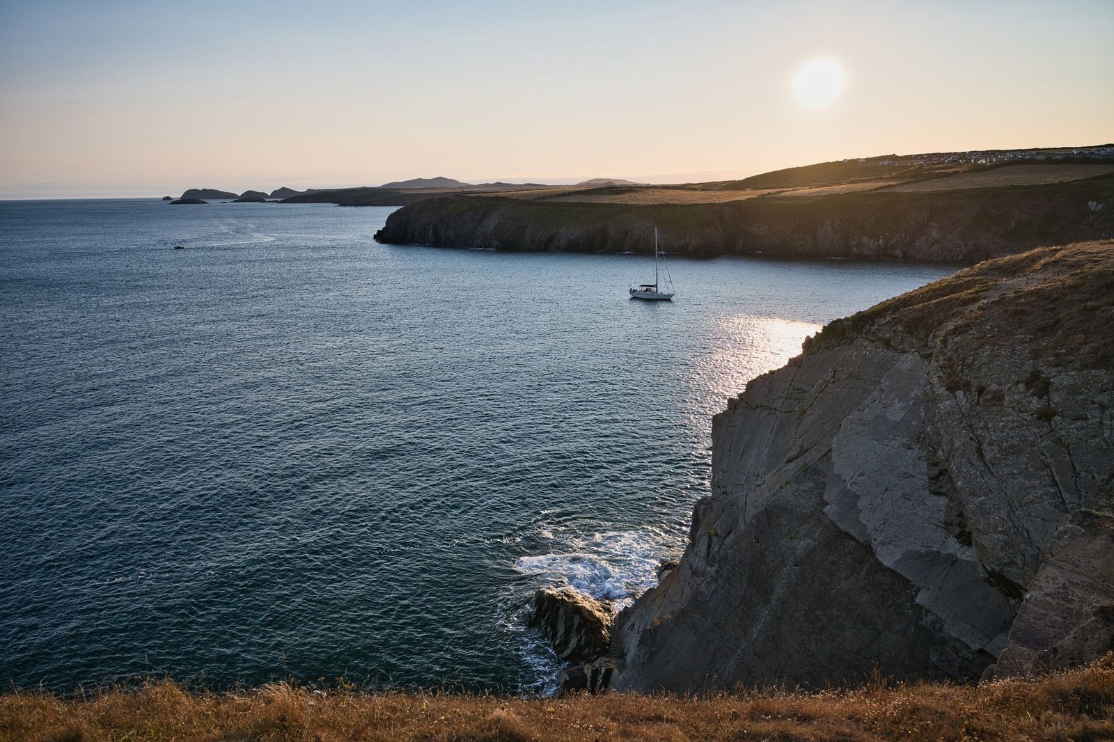Breathtaking coastal scene in Wales with a sailboat and sunset over the ocean, perfect for travel inspiration.