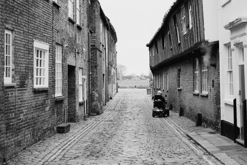 Historic cobblestone alley in King's Lynn featuring old brick buildings and a solitary figure in an electric wheelchair.
