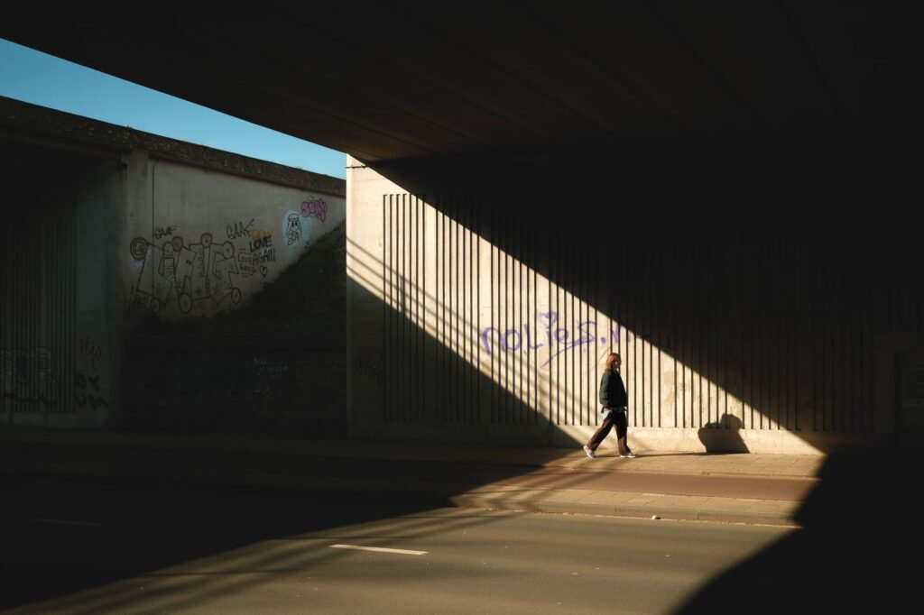 A person walks under an urban tunnel, casting shadows against graffiti-covered walls.