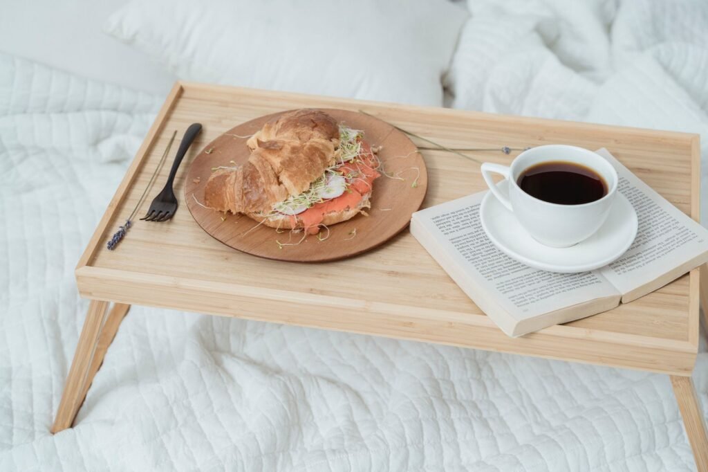A cozy breakfast in bed featuring a croissant sandwich with fresh coffee on a wooden tray.