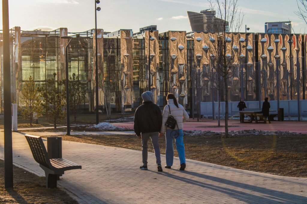 A couple walks in a modern urban park during sunset with contemporary architecture in the background.