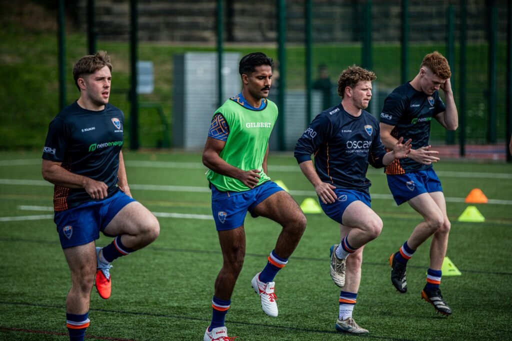 Four rugby players warming up during a practice session on an artificial grass field in Birmingham.