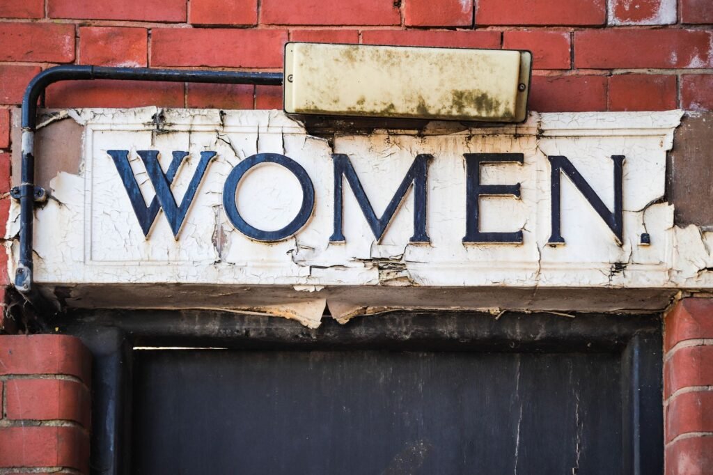 Close-up of a vintage 'Women' restroom sign on a brick wall in Birmingham, England.