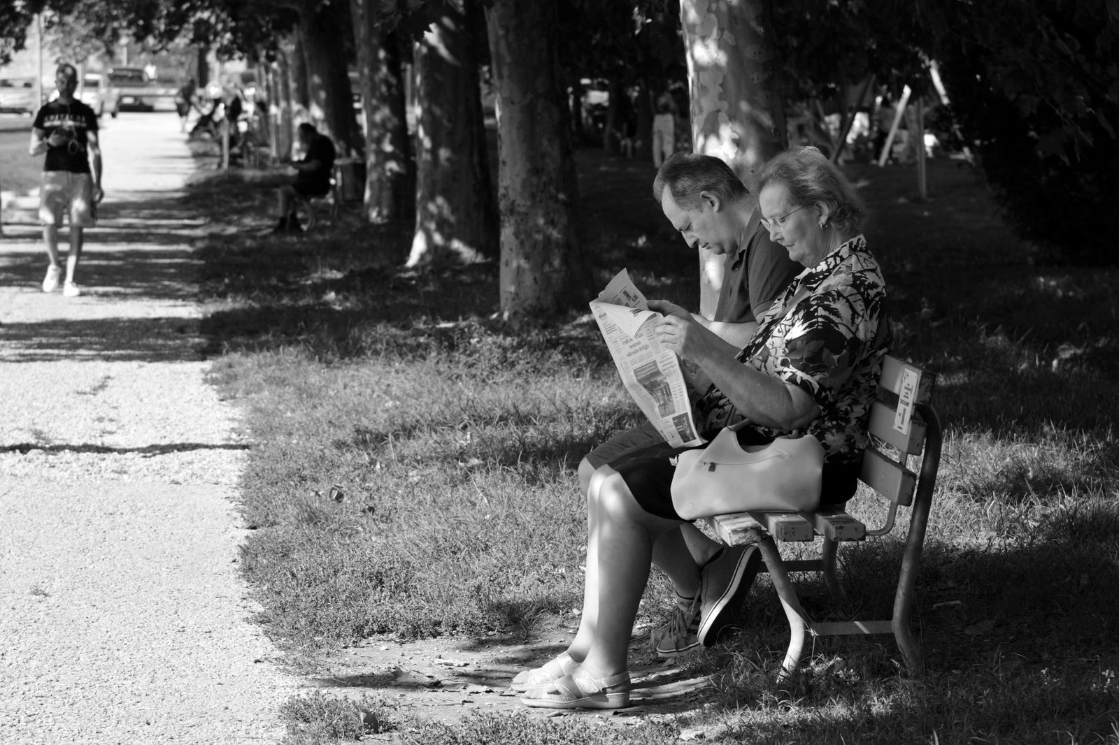 Senior couple reading in a shady Verona park during the day, captured in black and white.