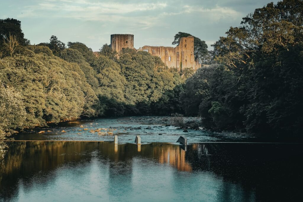 Capture of Barnard Castle ruins set amid a lush, tranquil summer landscape reflecting on a serene river.
