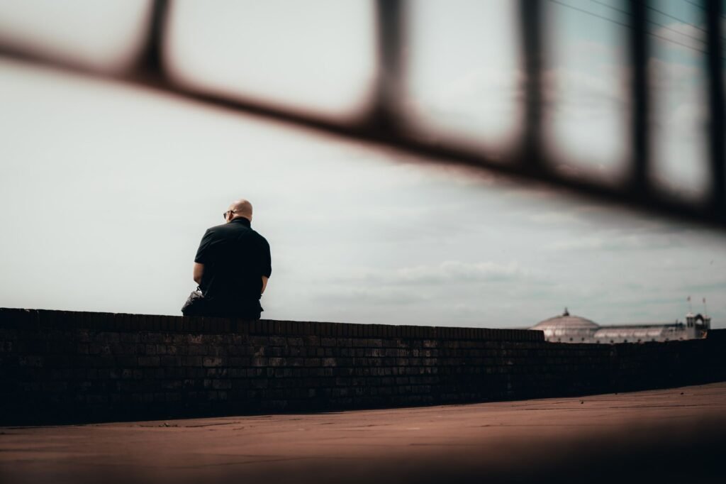 A solitary man sits contemplatively on a wall in Brighton and Hove, England.