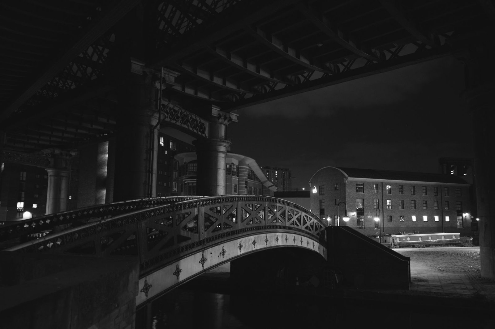A black and white nighttime view of a historic bridge in Manchester, UK, showcasing architectural elegance.