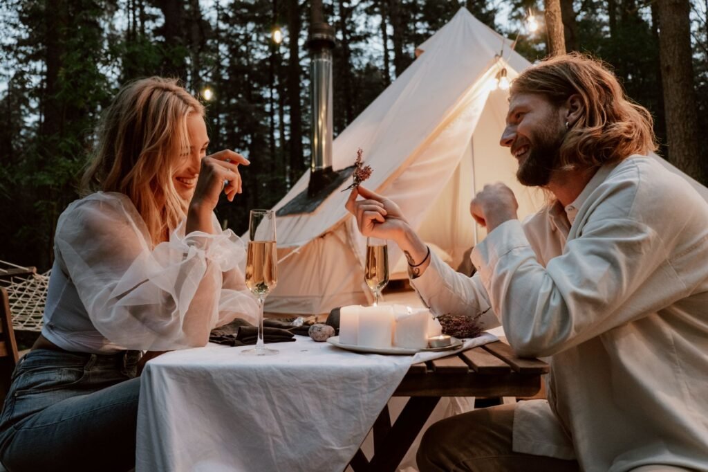 A couple enjoys a romantic evening picnic with champagne in a forest setting.