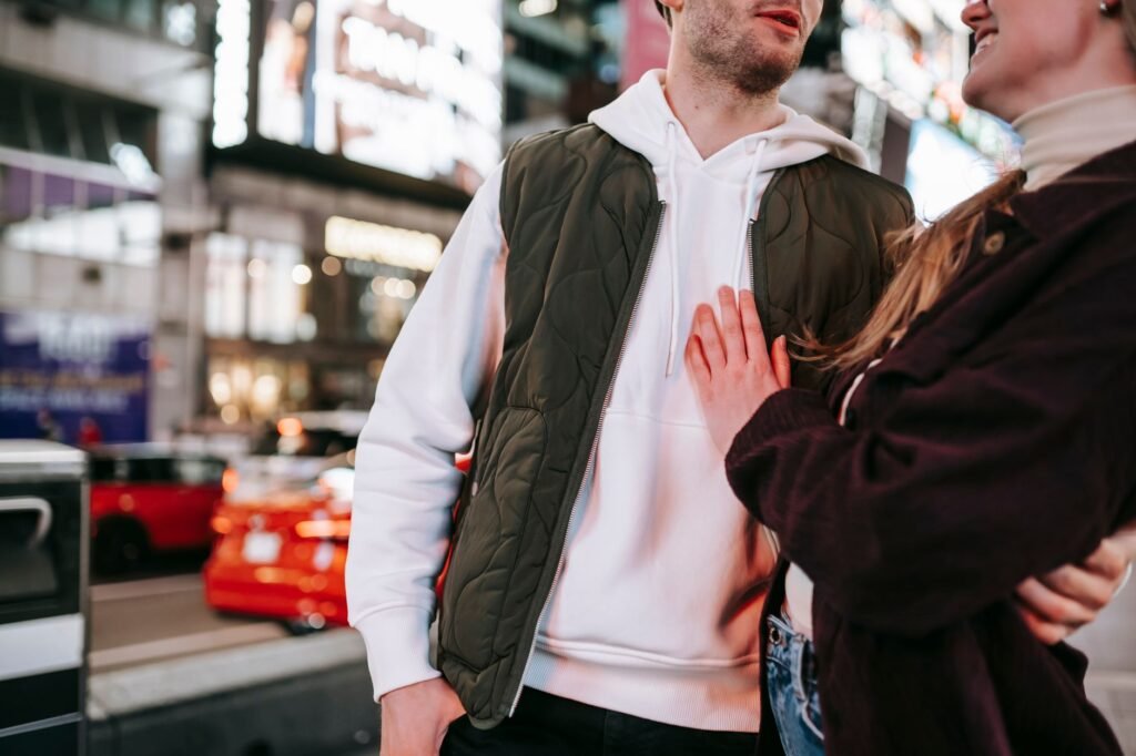 Unrecognizable couple embracing while standing on street near road against glowing signboards on modern buildings and cars on