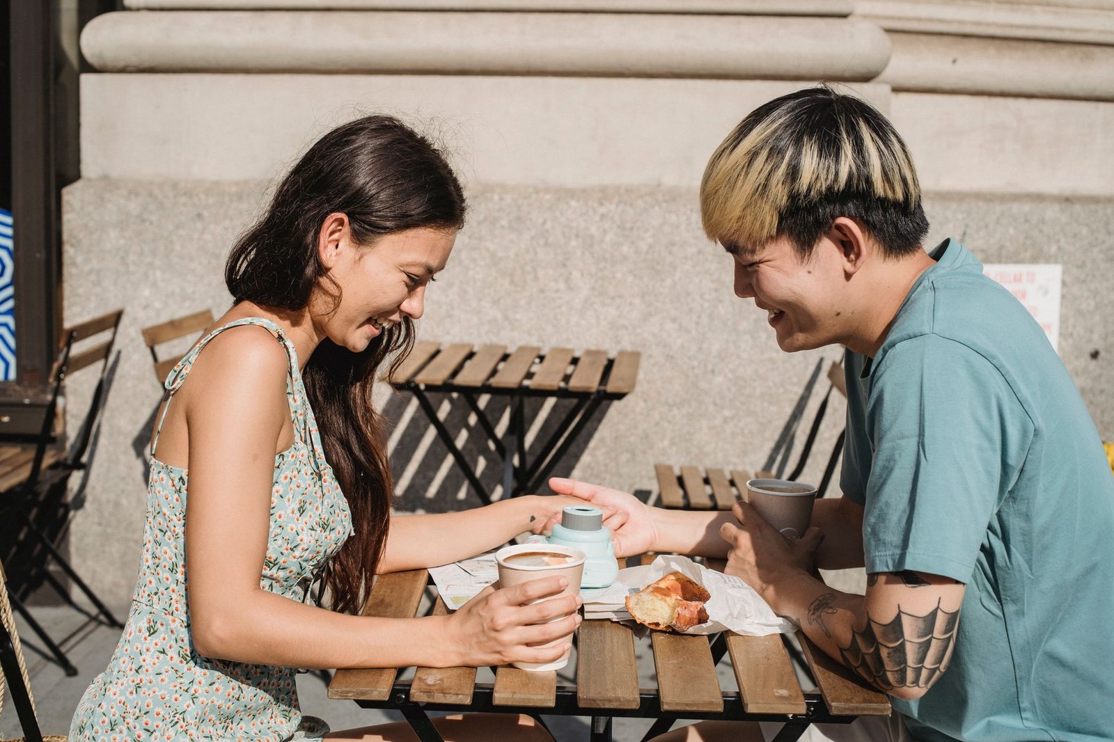 Side view of young multiracial couple drinking coffee and holding hands at table on street