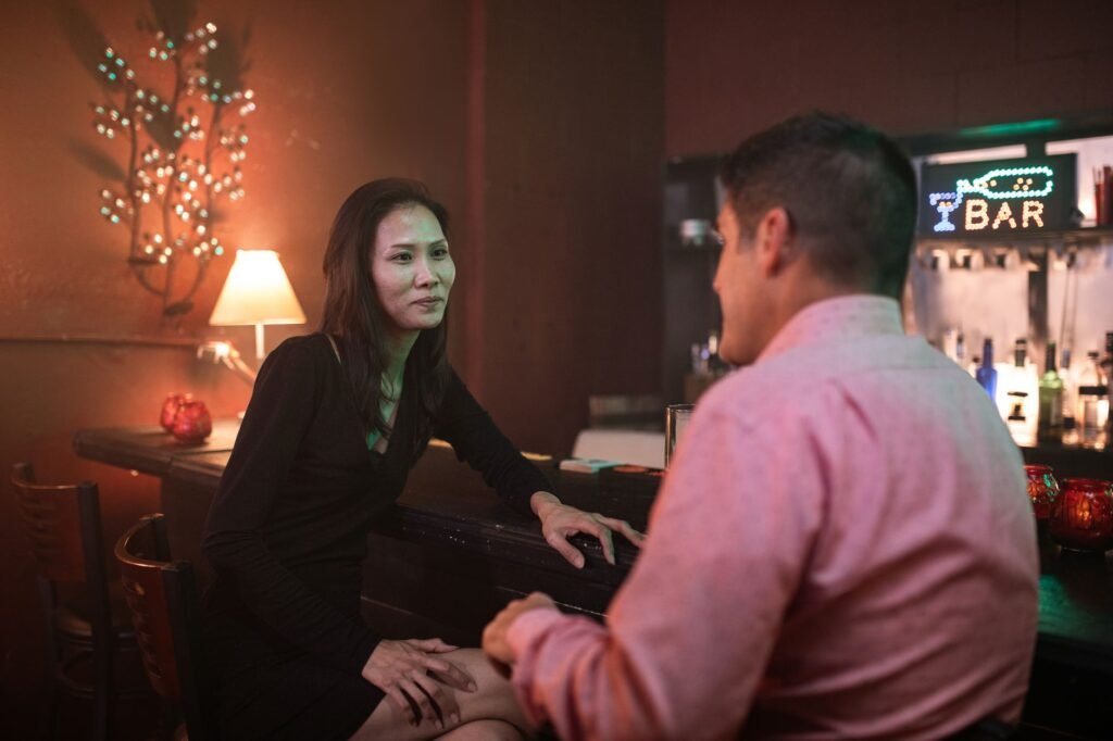 An Asian woman and a man enjoying a conversation at a stylish bar during the night.
