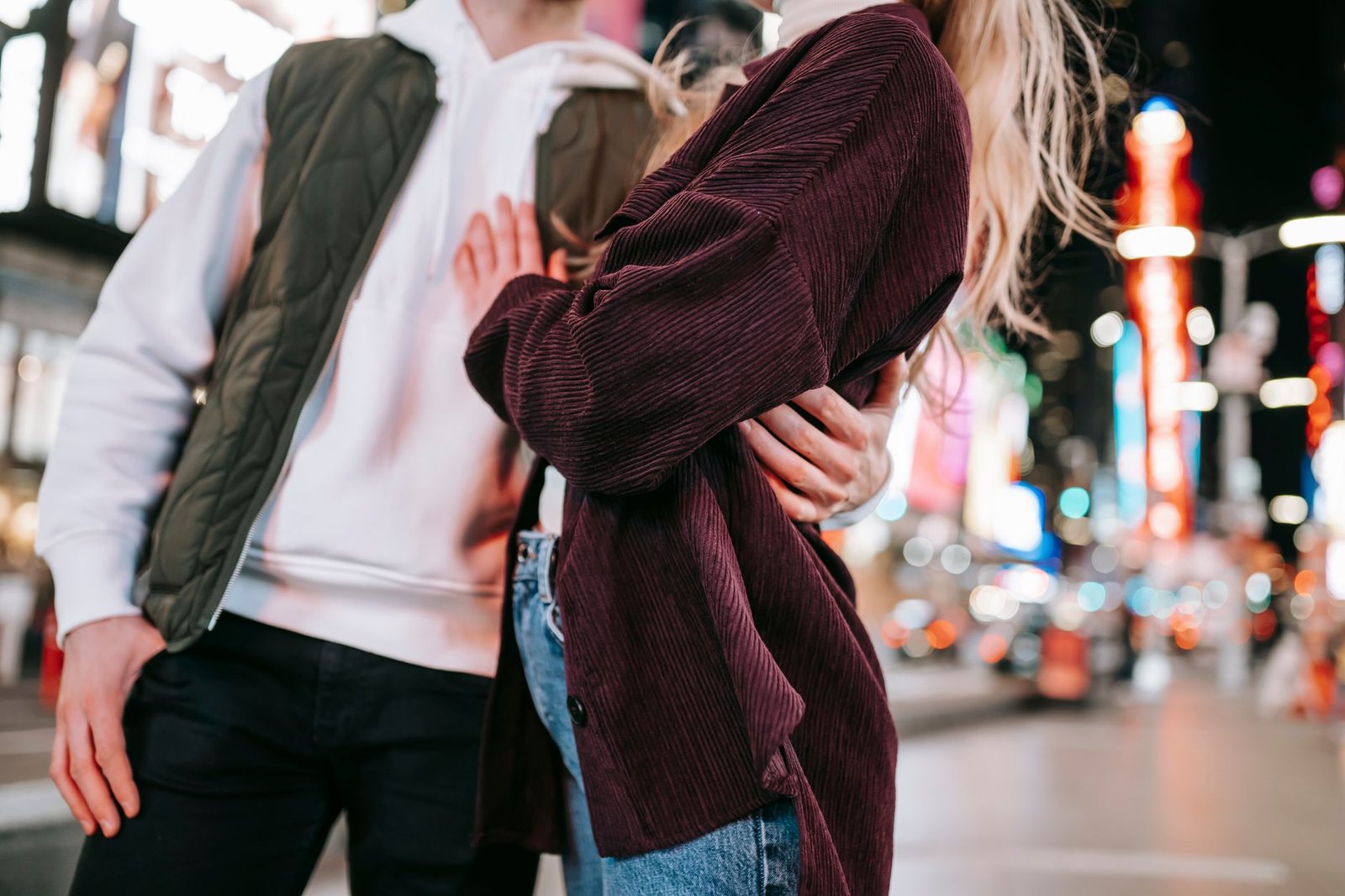 Unrecognizable loving couple embracing gently while standing on roadside of city with glowing cars and modern skyscrapers on