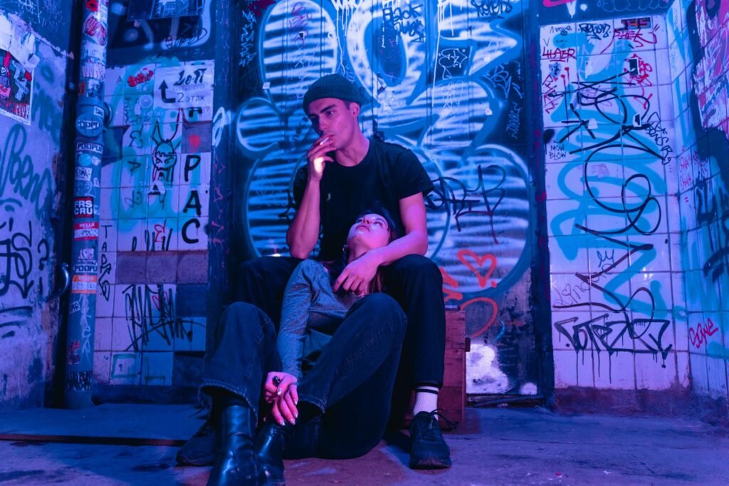 Couple sitting against graffiti wall in alley, with a smoky neon-lit urban vibe.