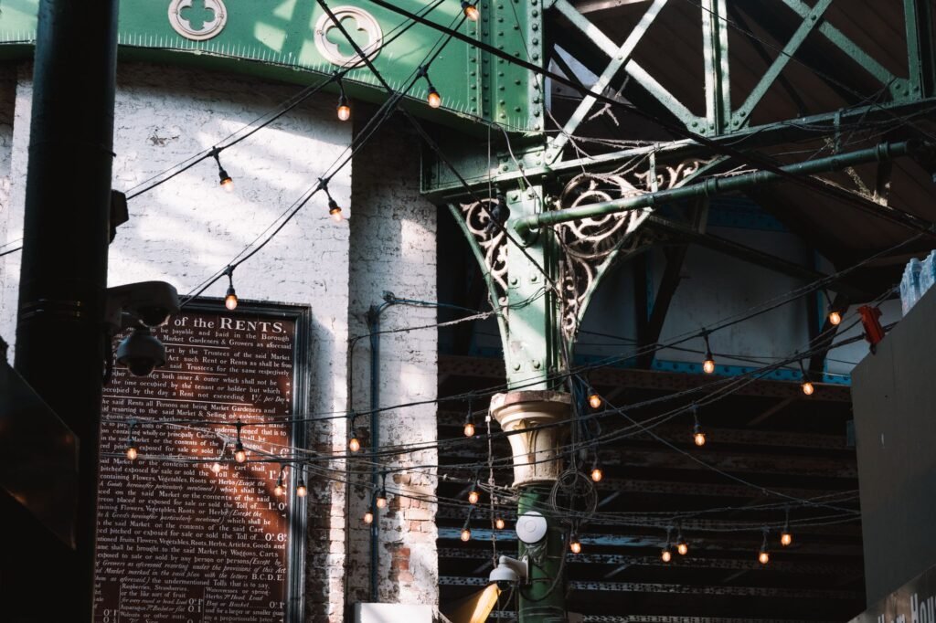 Intricate ironwork beams and string lights create a vintage urban atmosphere in London's historic district.