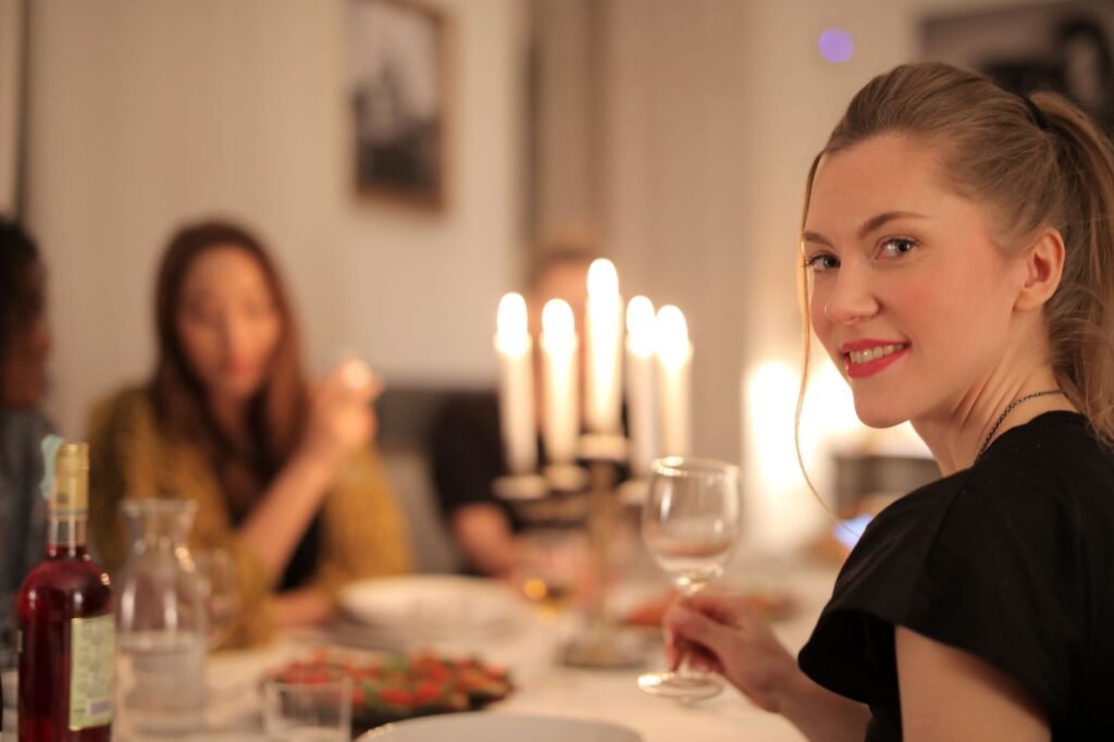 Smiling women enjoying a candlelit dinner with friends, sharing wine and laughter indoors.