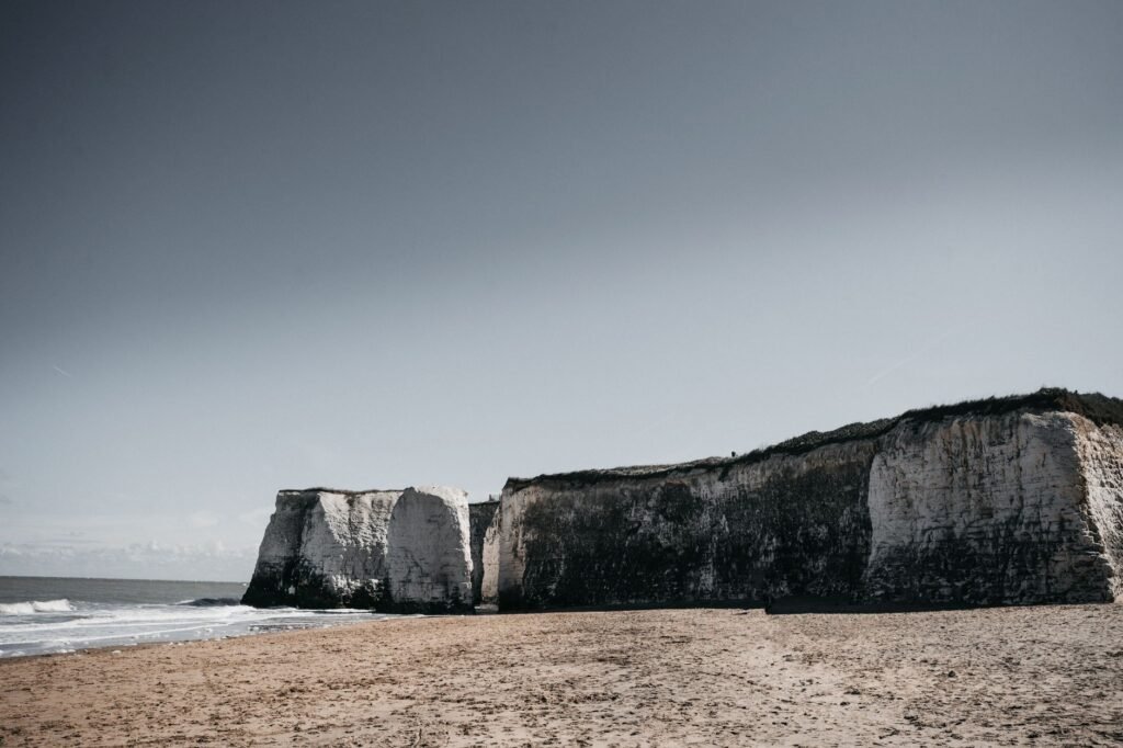 Majestic chalk cliffs overlooking a serene sandy beach on a clear day in Kent, England.