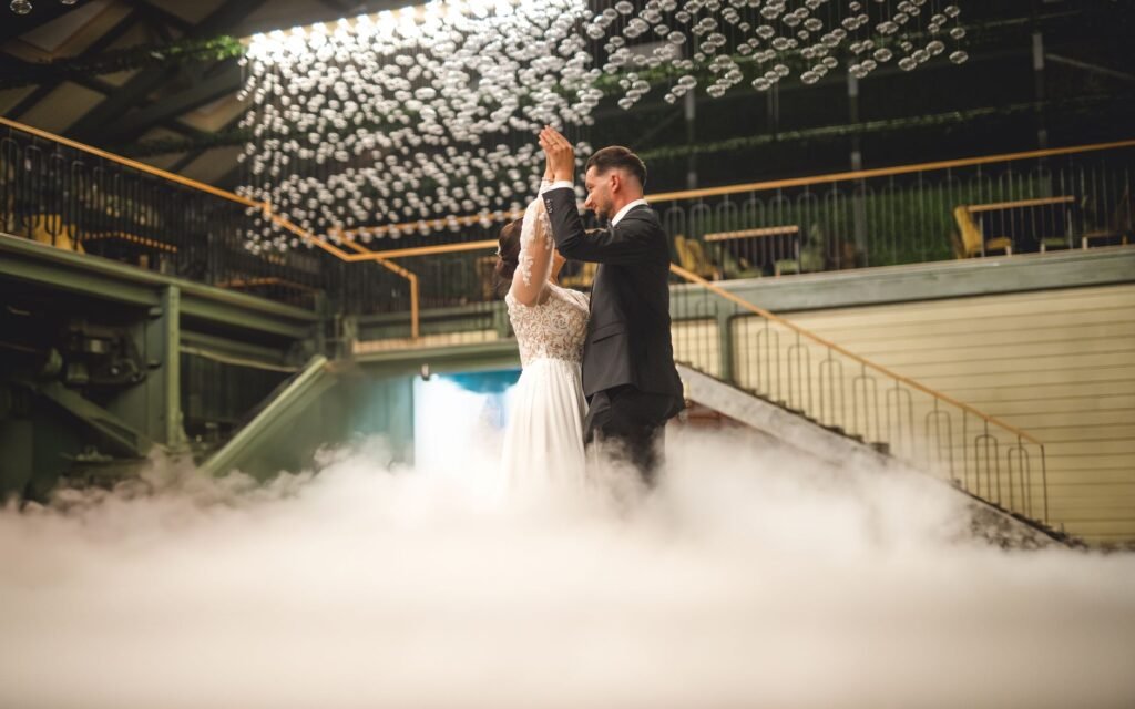 A couple shares a romantic dance at their wedding surrounded by mist and elegant decor.