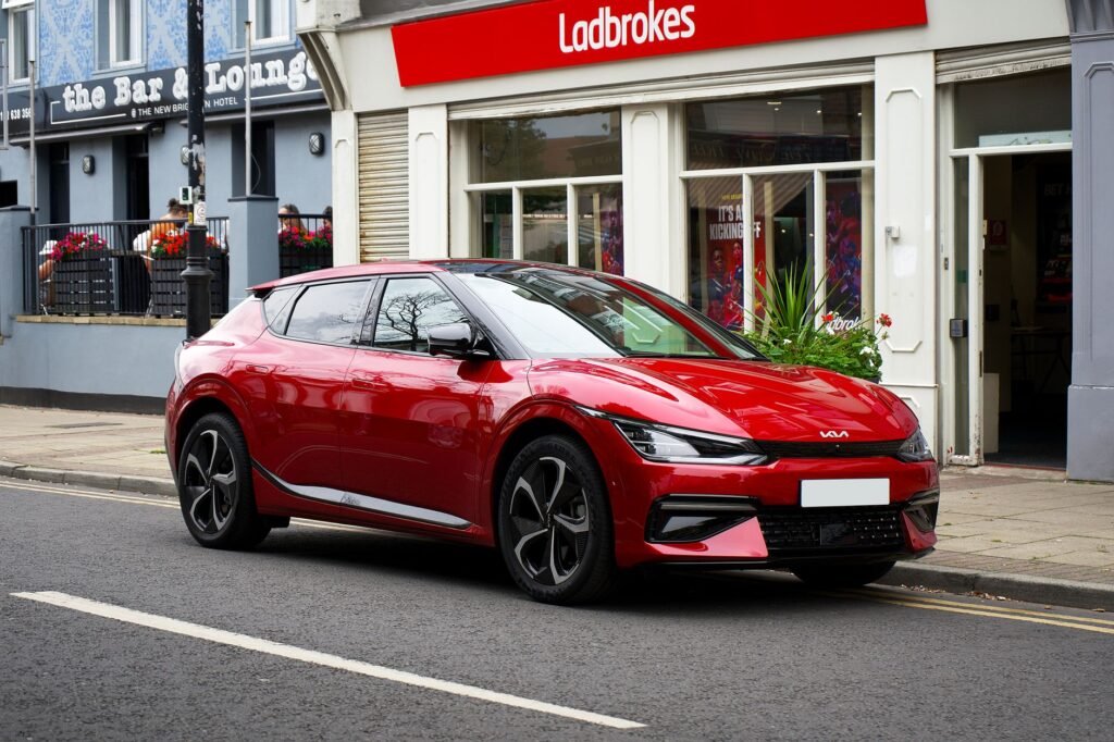 A sleek red electric car parked in front of shops in Liverpool, UK, showcasing urban street life.