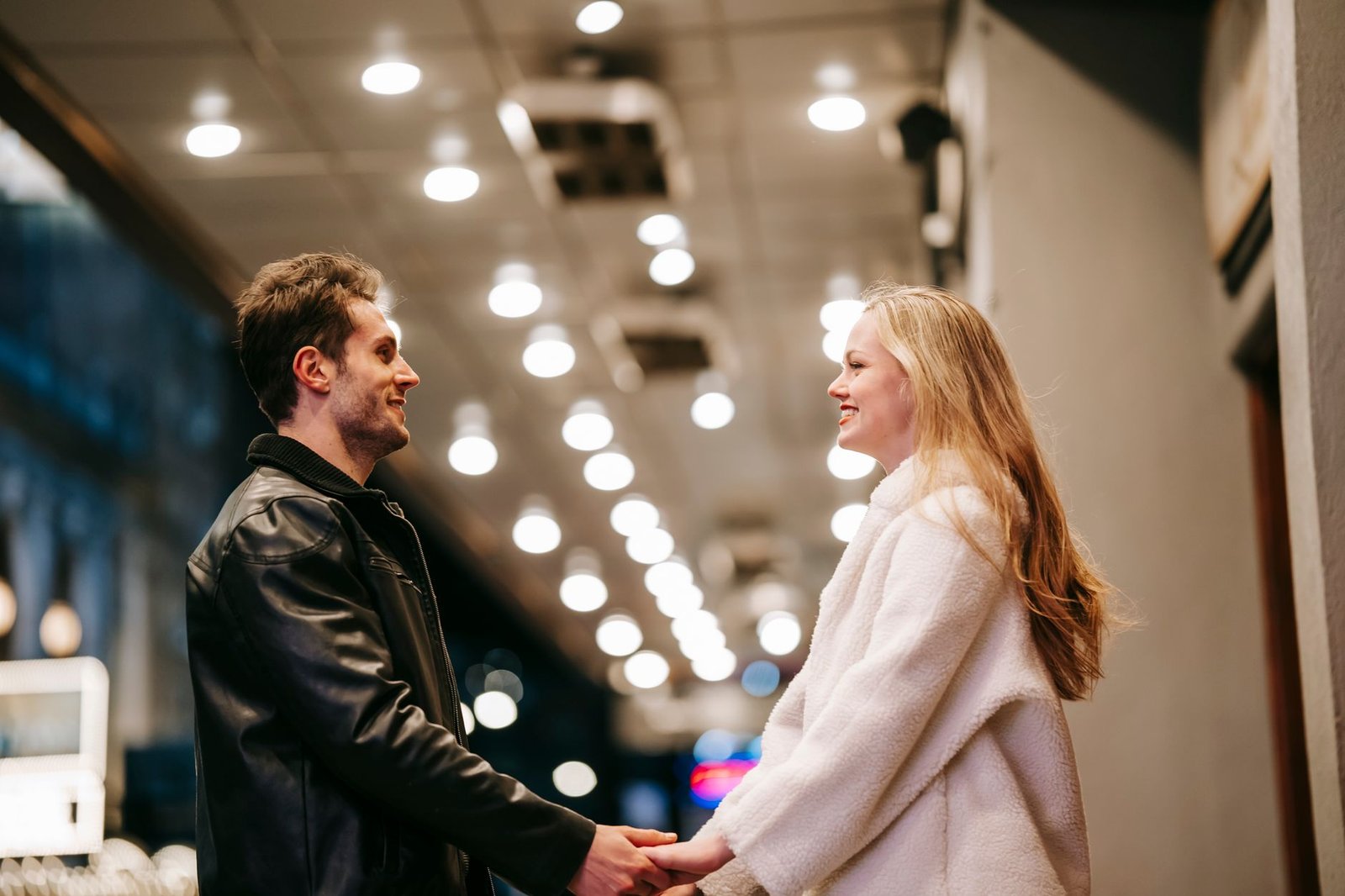 Side view low angle of positive couple holding hands and looking at each other while standing in corridor of subway station w