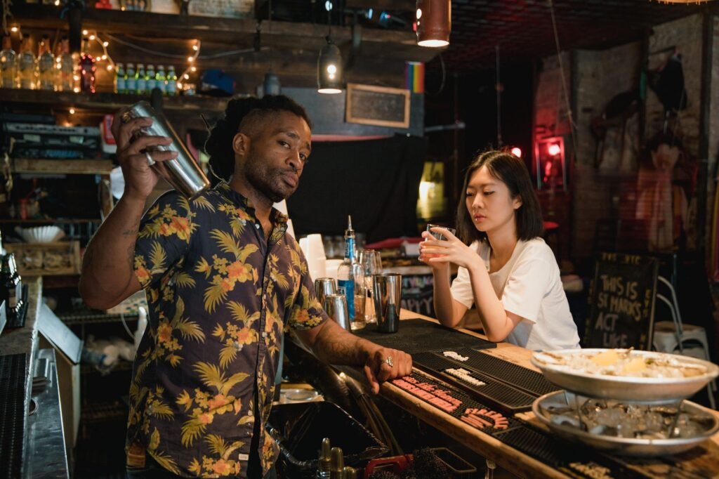 A bartender in a Hawaiian shirt preparing a cocktail for a customer at a dimly lit bar.