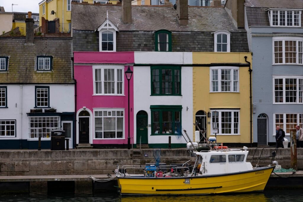 A vibrant fishing boat docked in front of colorful houses by the harbor in Weymouth, England.