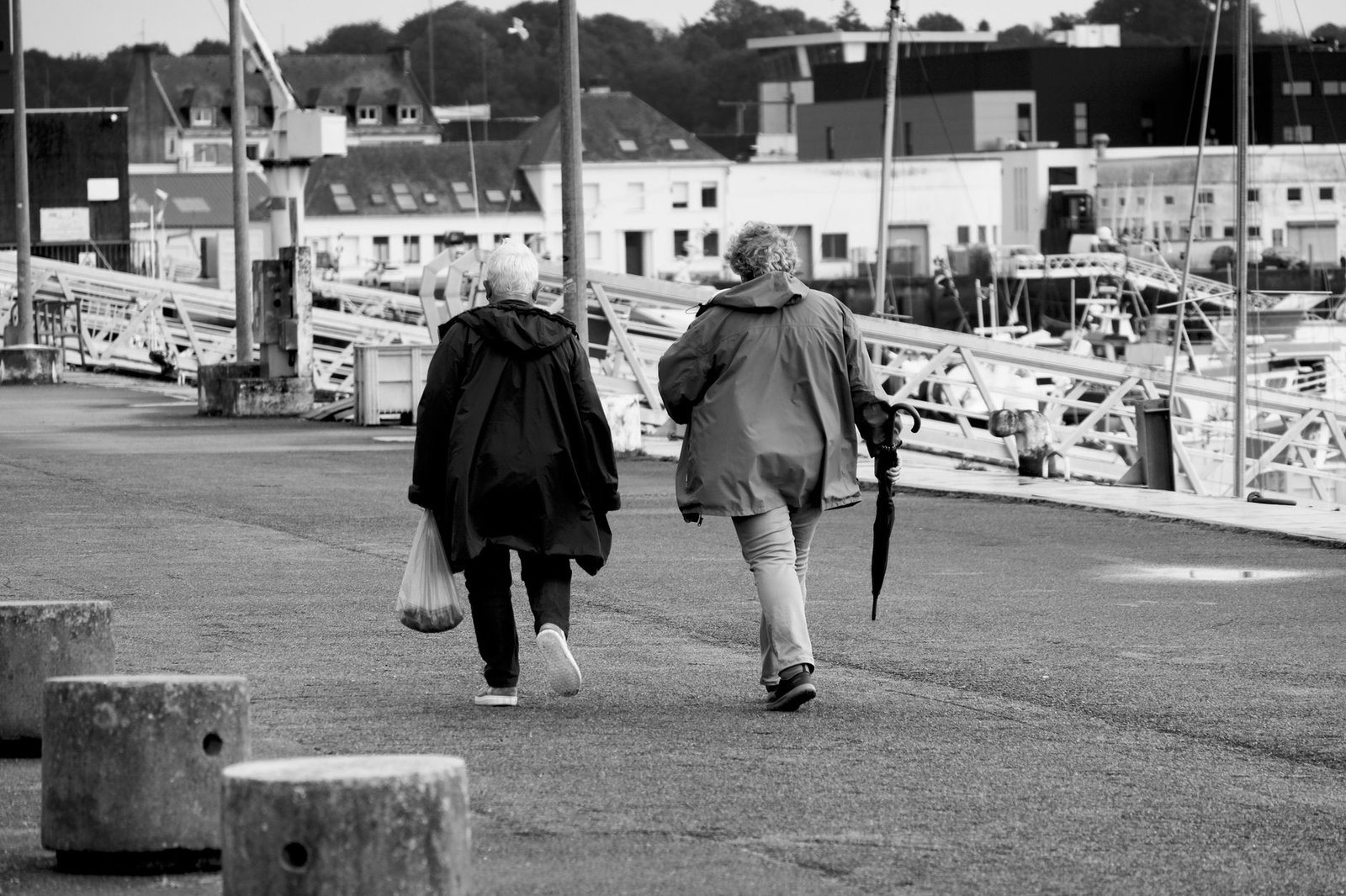 Two senior adults walk along a city waterfront with buildings in the background.