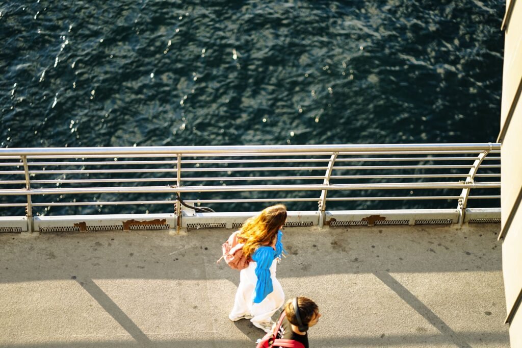 Top-down view of two women walking along a waterfront pier on a sunny day.