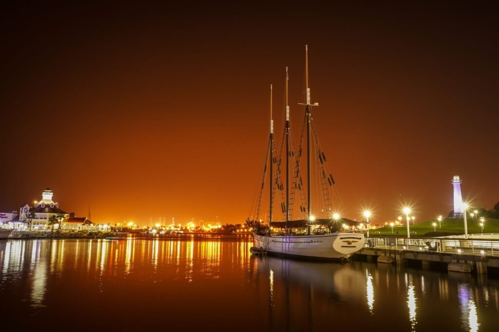 A calm night at Long Beach Harbor featuring a docked sailboat and waterfront cityscape lighting.
