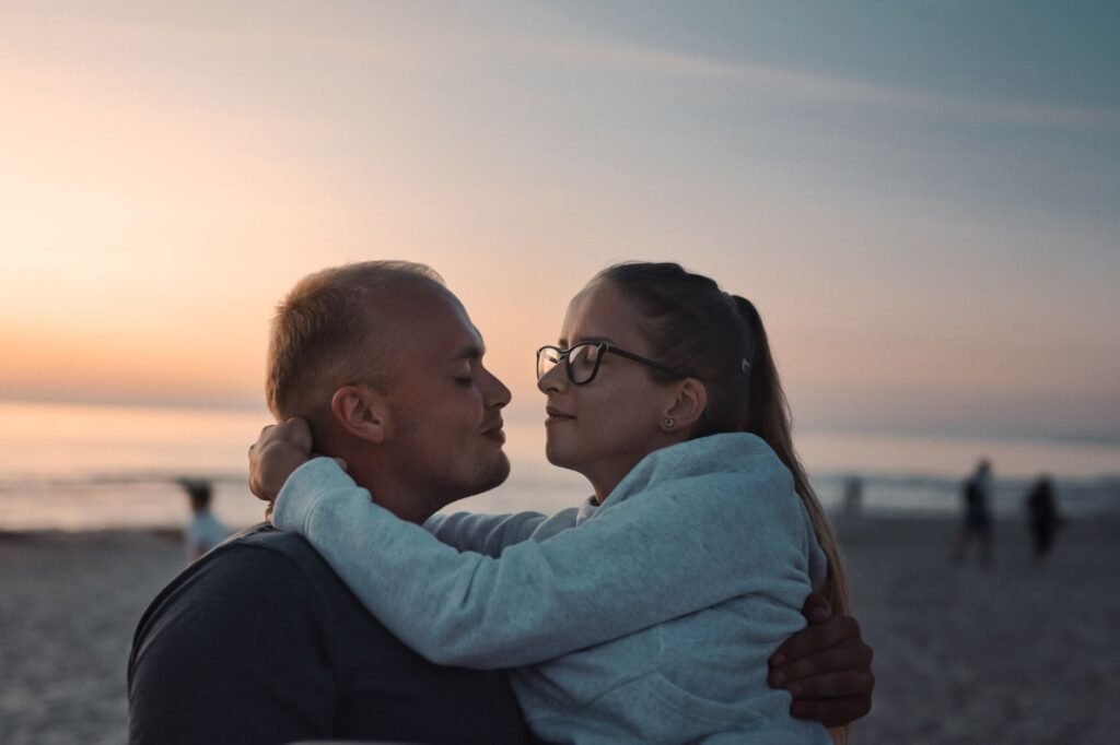 A couple embraces on a beach during a warm sunset, showcasing love and togetherness.