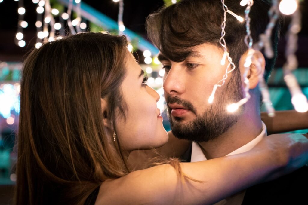 Close-up of a young couple embracing and gazing at each other romantically under string lights.