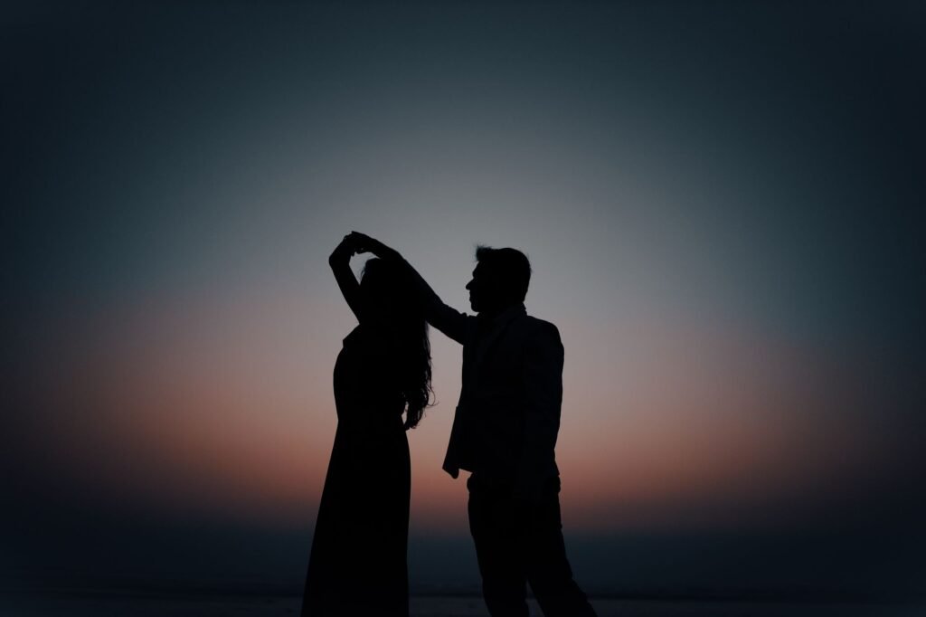 Romantic silhouette of a couple dancing gracefully against a vibrant sunset backdrop.