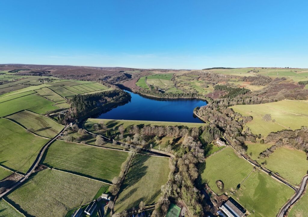 Aerial shot of Damflask Reservoir surrounded by lush green fields and rural landscape in South Yorkshire.
