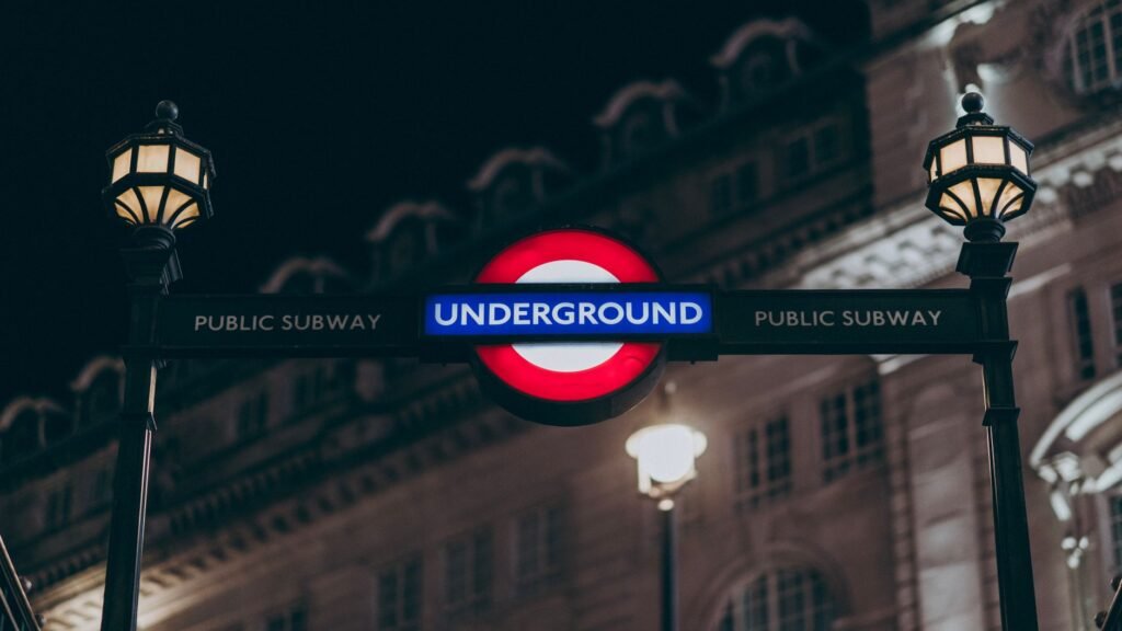 Illuminated London Underground sign with lamp posts at night.