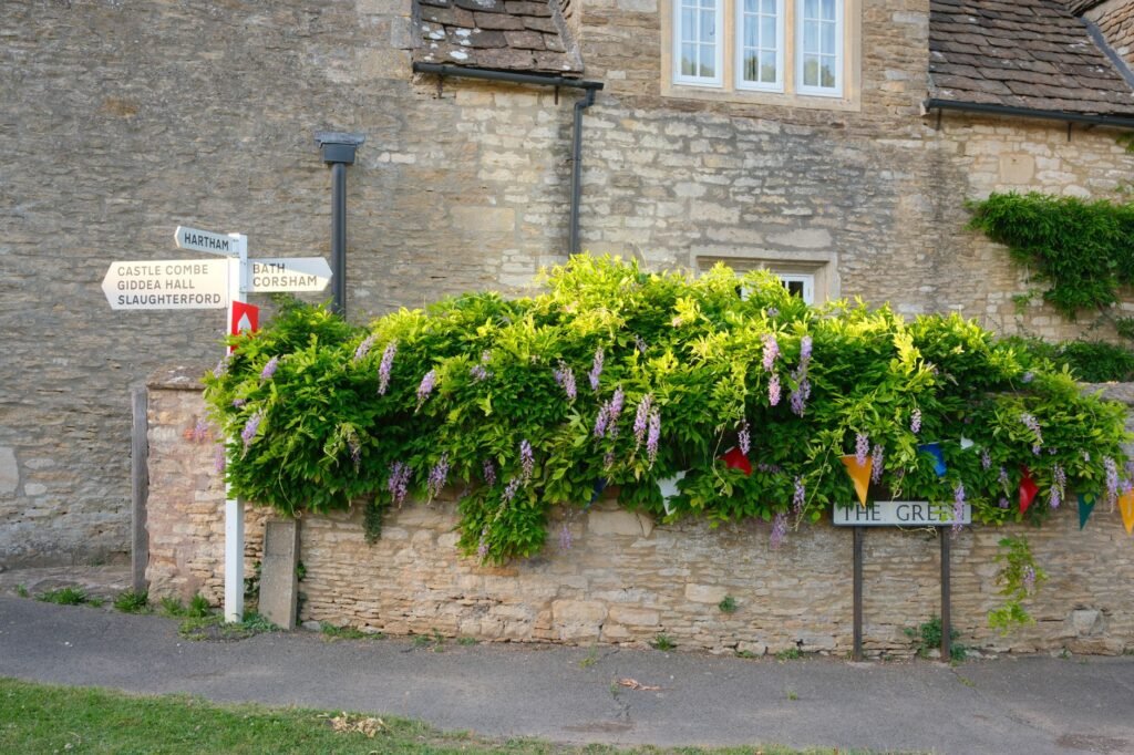Picturesque stone house with vibrant greenery and directional signs in Biddestone, England.