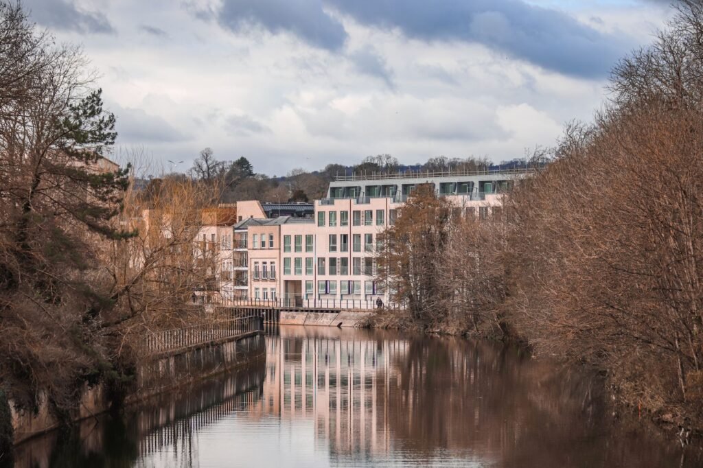 A beautiful view of modern buildings along a river with winter trees and reflections.