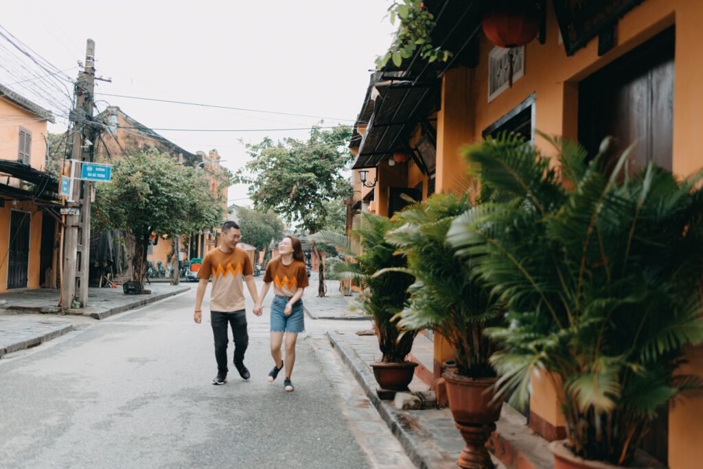 Full body of young ethnic couple promenading on street with small houses and plants with fresh verdant leaves