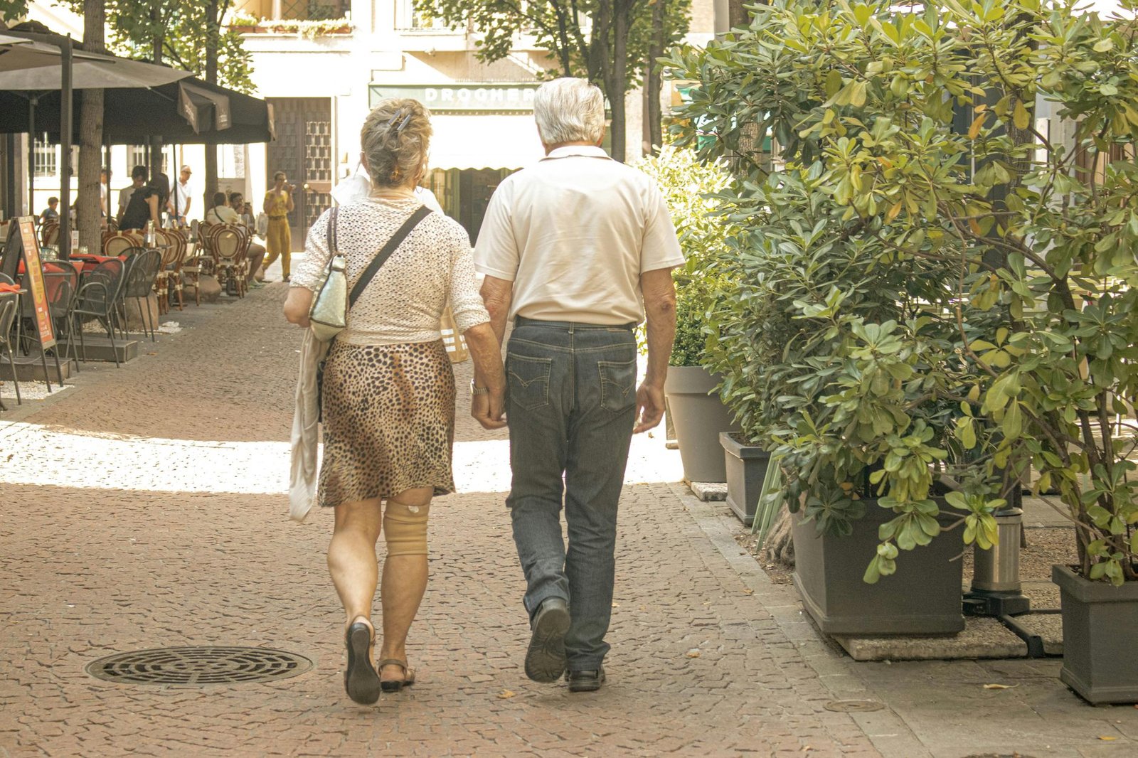 An elderly couple strolling hand in hand down a charming street in Italy.