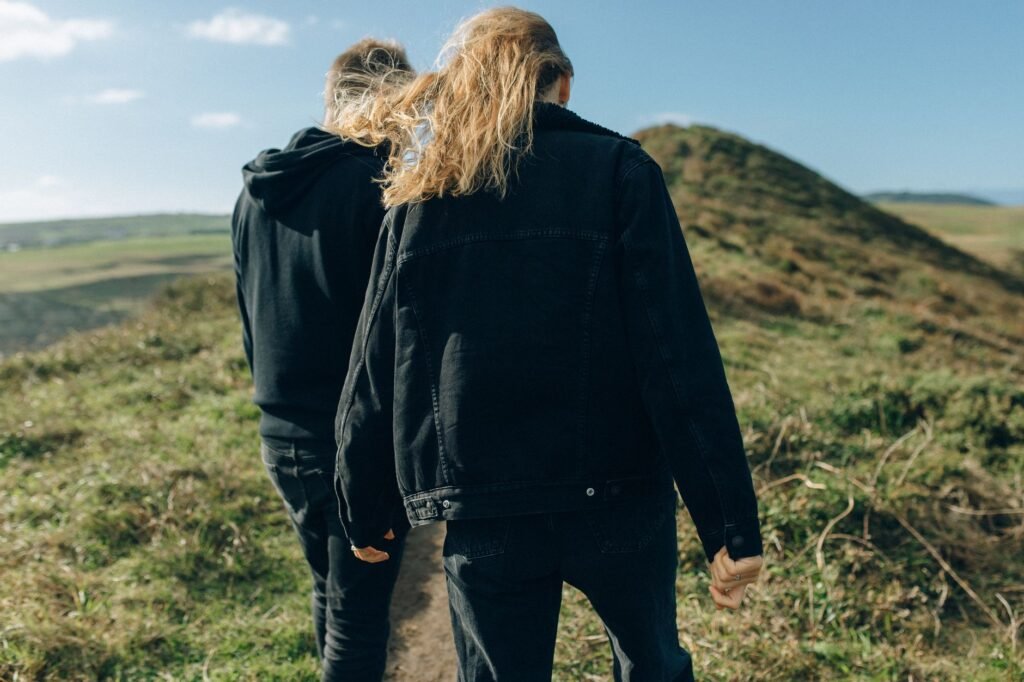 A couple enjoying a scenic hike on a grassy mountain trail under a clear blue sky.