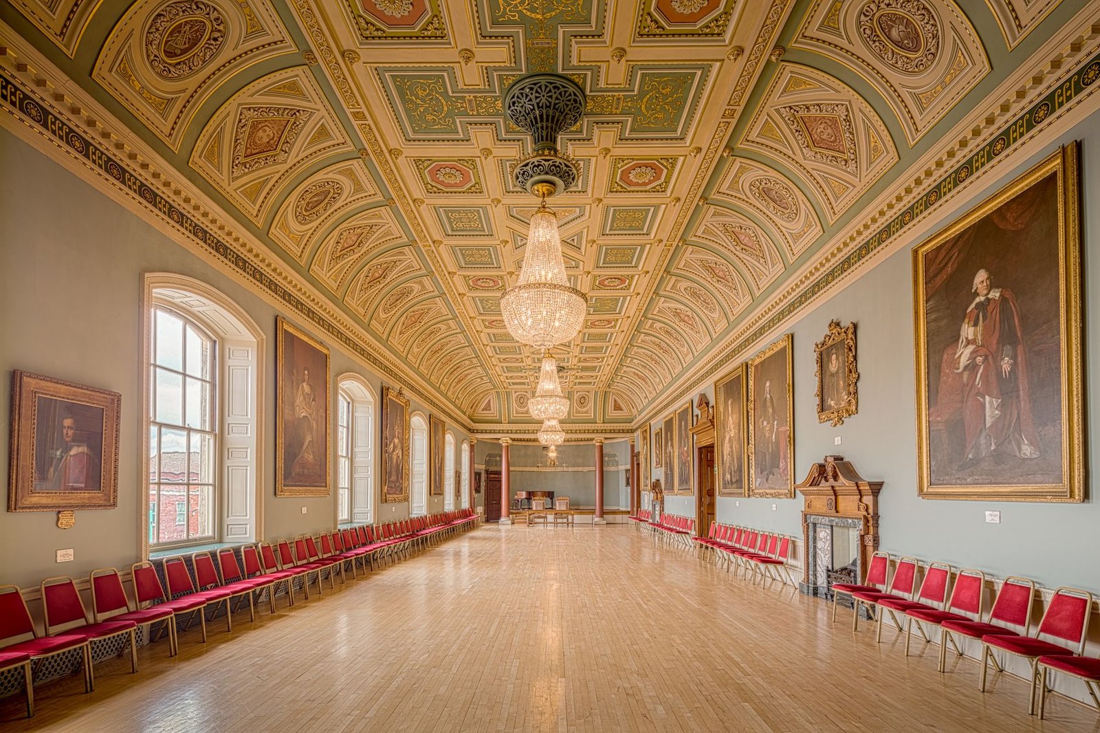 A beautifully preserved historical guildhall interior with ornate chandeliers and large portraits, located in England.