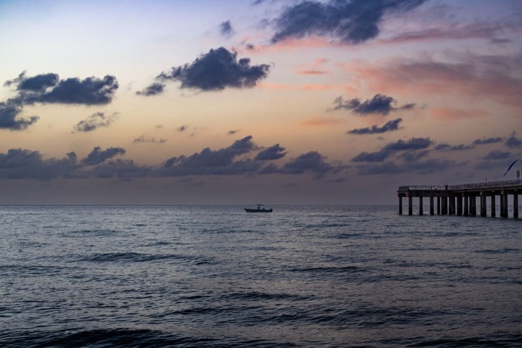 Serene sunset scene at Miami Beach with a distant boat and pier silhouetted against the colorful sky.