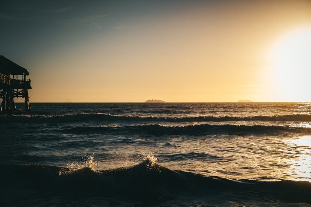 Peaceful sunset view over the ocean at Cocoa Beach, Florida with a silhouetted pier and gentle waves.