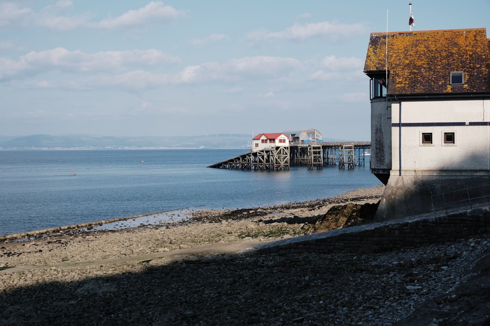 Tranquil coastal scene with pier and historic building under blue sky.